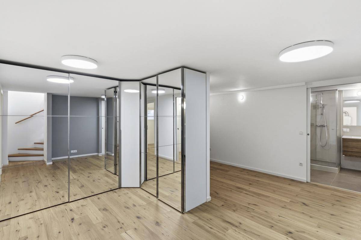 Geräumiges Schlafzimmer mit Holzboden, Spiegelschränken und angrenzendem Badezimmer.