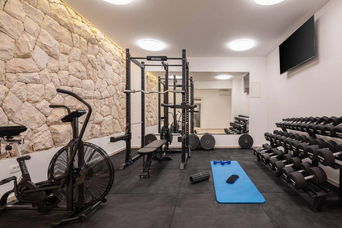 Gut ausgestatteter Fitnessraum mit verschiedenen Trainingsgeräten, Hanteln und einer Steinwand.
