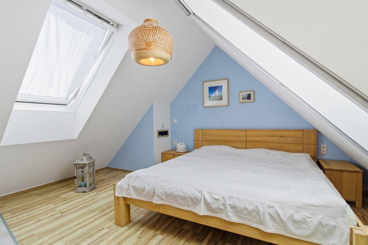 Helles Schlafzimmer mit Holzbett, blauer Akzentwand, Holzboden und einem großen Dachfenster.