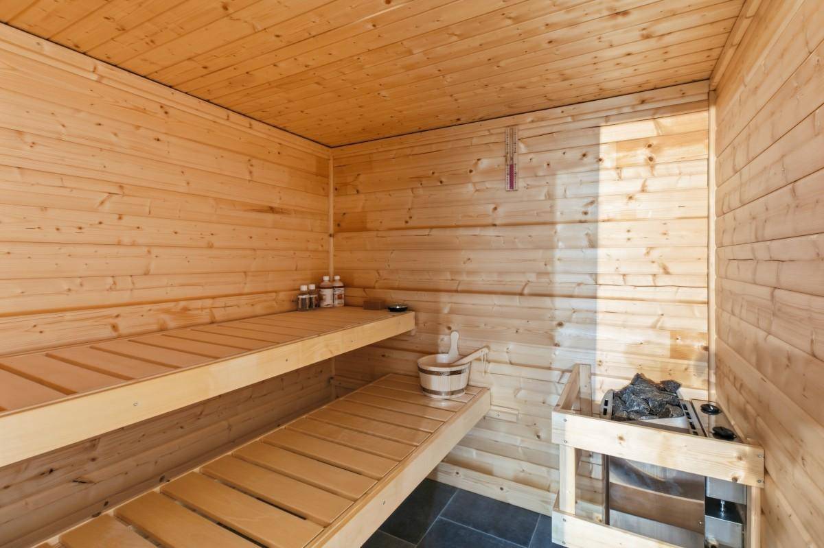 Innenansicht einer traditionellen Holzsauna mit Sitzbänken und einem Saunaofen.