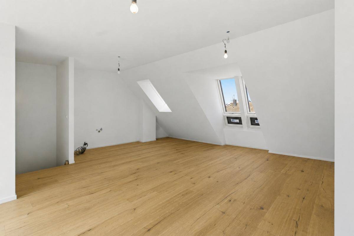Heller Dachgeschossraum mit Holzboden und schrägen Wänden, ausgestattet mit zwei Dachfenstern für Tageslicht.