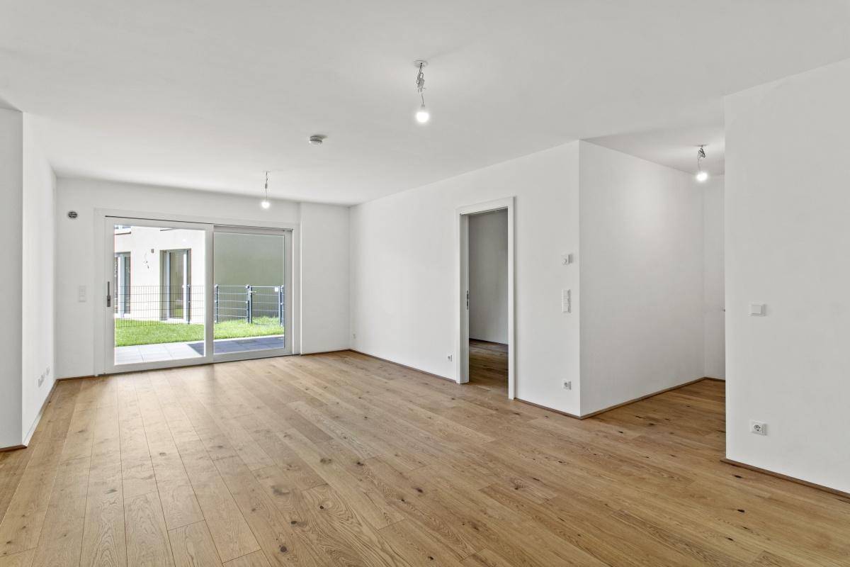 Helles, leeres Wohnzimmer mit Eichenparkett und großem Schiebetürzugang zum Garten.