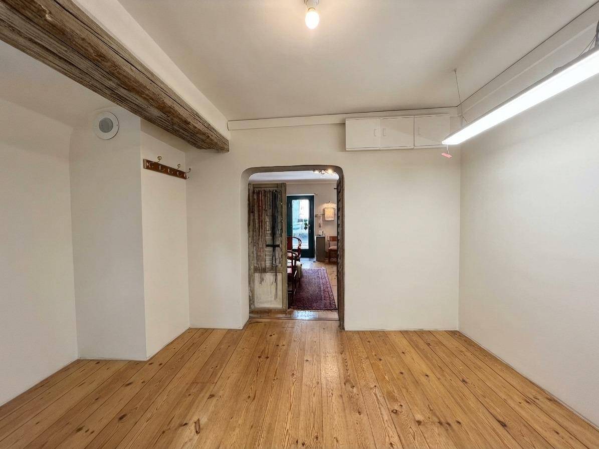 Innenraum mit Holzdielenboden, sichtbaren Holzbalken an der Decke und einem Durchgang zu einem weiteren Bereich.