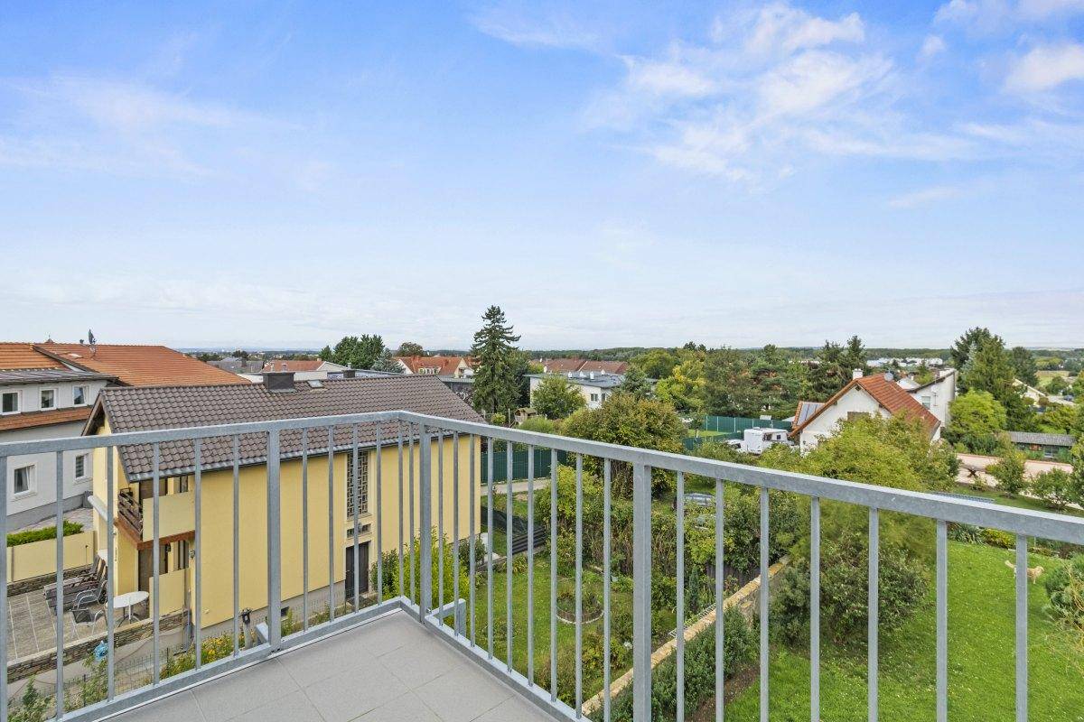 Blick von einem Balkon mit Metallgeländer über eine Wohnsiedlung und grüne Landschaft.