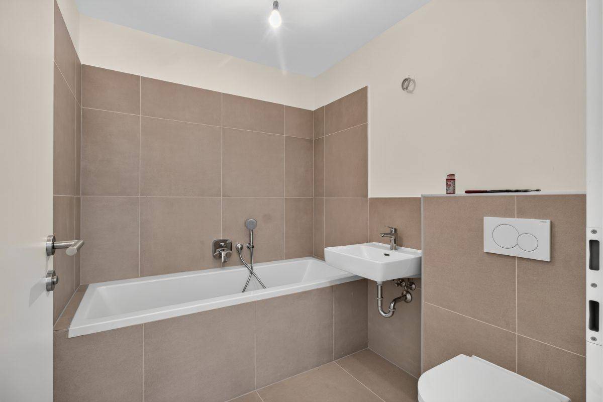 Badezimmer mit Badewanne, Waschbecken und WC, ausgestattet mit beigen Fliesen.