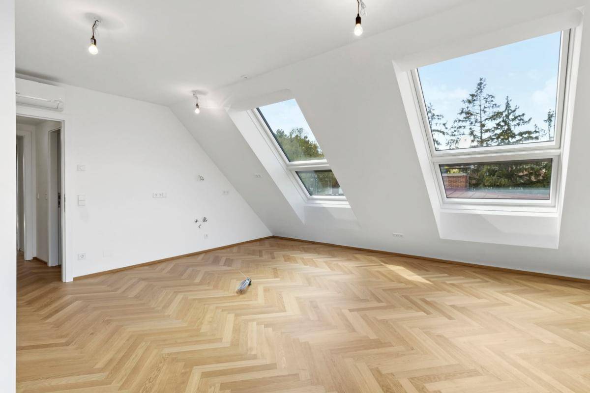 Heller Wohnraum mit Fischgrätparkett und großen Dachfenstern unter schrägen Decken.