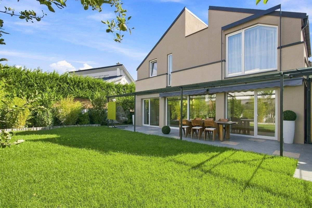 Gepflegter Garten mit Rasenfläche und einer möblierten Terrasse unter einer Pergola.