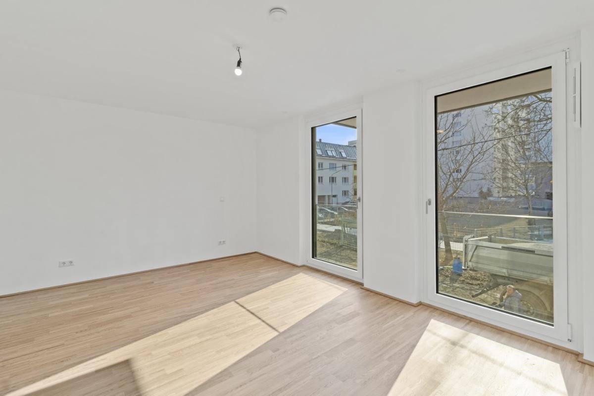 Heller Raum mit Holzboden und großen Fenstertüren, die Zugang zu einem Balkon bieten.