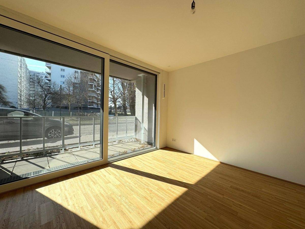 Helles, leeres Zimmer mit Parkettboden und Zugang zu einem Balkon.