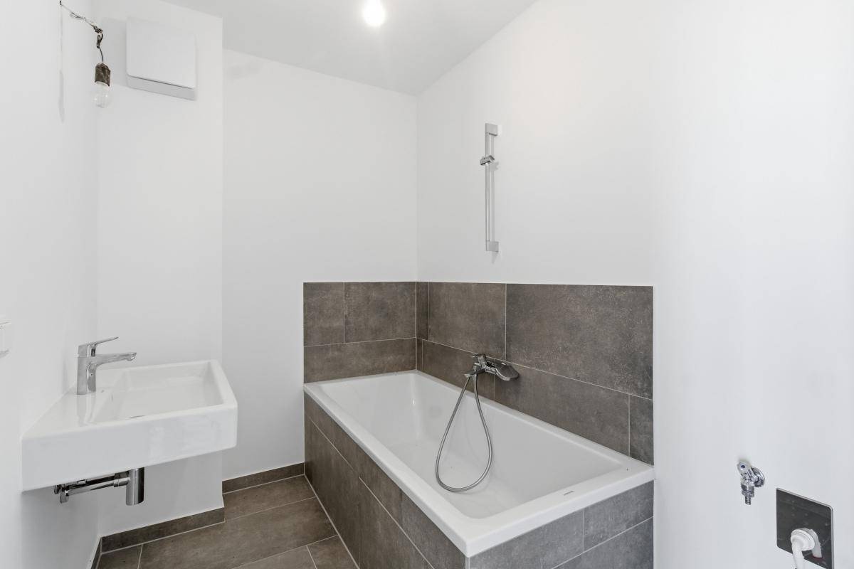Modernes Badezimmer mit Badewanne, Waschbecken und grauen Fliesen.