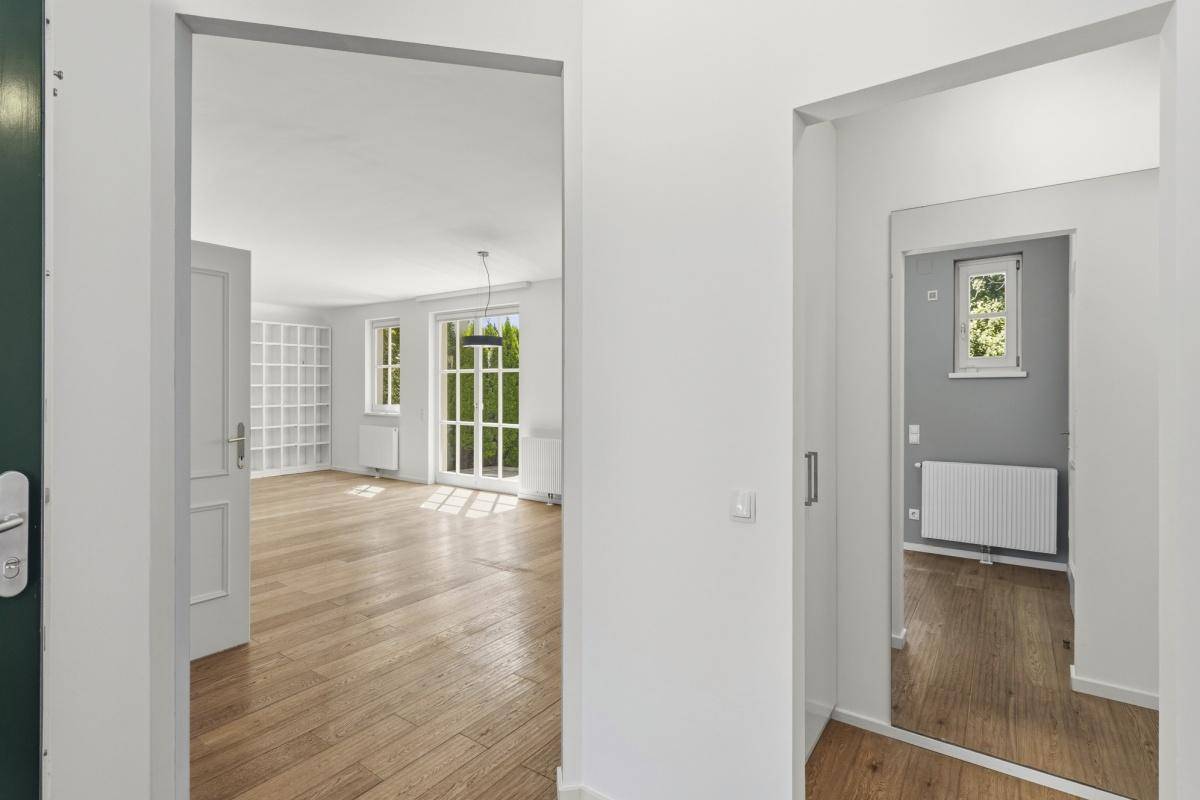 Geräumiger Flur mit Holzboden und Durchgang zu einem hellen Wohnbereich mit Gartenzugang.