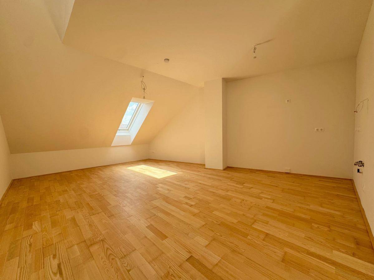 Geräumiger Dachgeschossraum mit Holzboden und einem einzelnen Dachfenster, hell und leer.