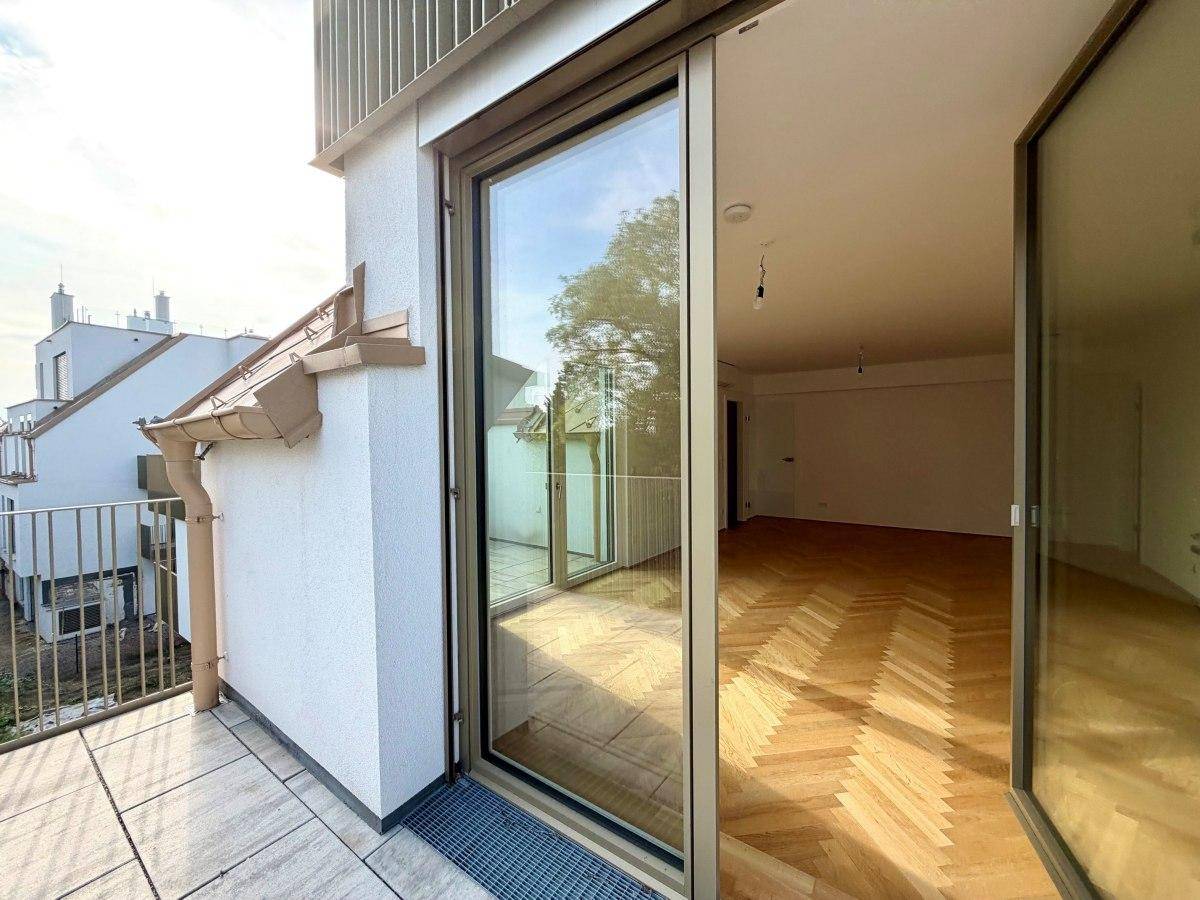 Blick vom Balkon in einen hellen Innenraum mit Fischgrätparkett durch eine große Schiebetür.