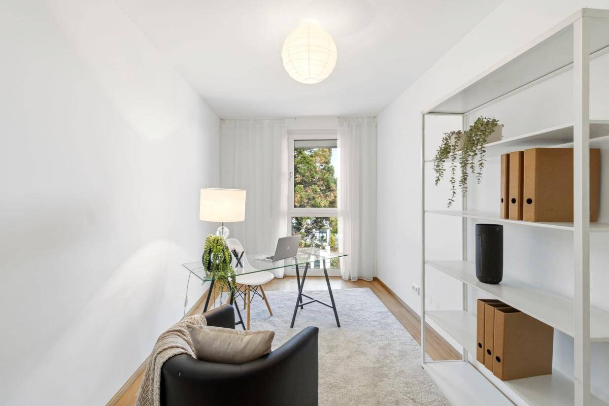 Modernes Arbeitszimmer mit Schreibtisch, Regal und Blick ins Grüne durch das Fenster.