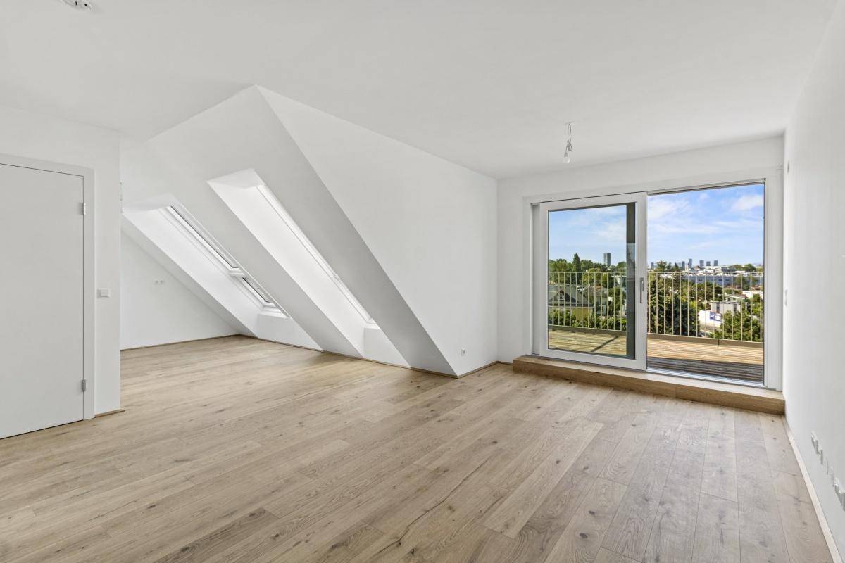 Lichtdurchfluteter Raum im Dachgeschoss mit Holzboden, Dachschrägen und Zugang zum Balkon.