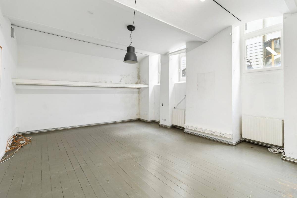 Leerer Gewerberaum mit grau gestrichenem Holzboden, weißen Wänden und einem Fenster, vielseitig nutzbar.