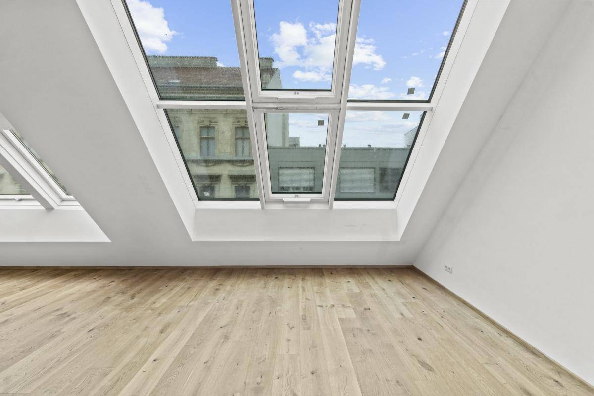 Lichtdurchfluteter Raum mit Holzboden und schrägen Wänden, ausgestattet mit großen Dachfenstern.