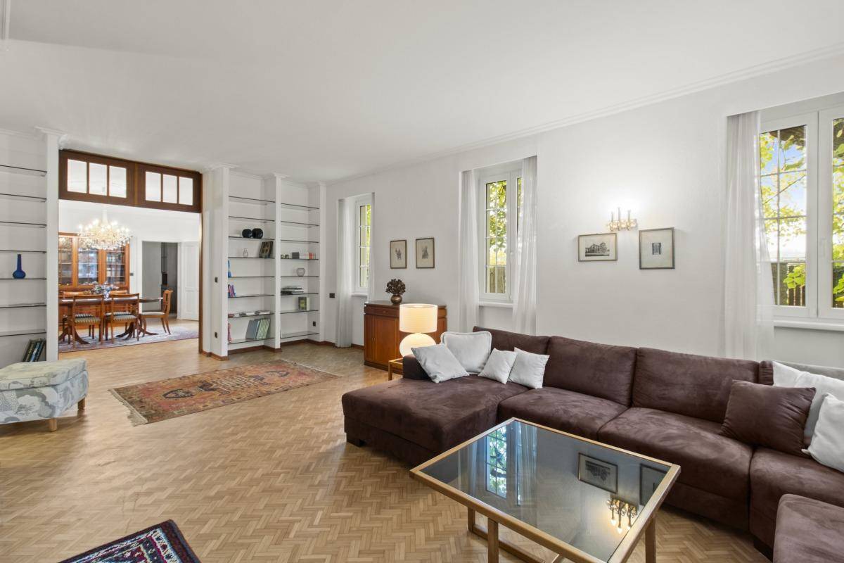 Helles Wohnzimmer mit braunem Ecksofa, Fischgrätparkett und Blick durch eine Holztür in den Essbereich.