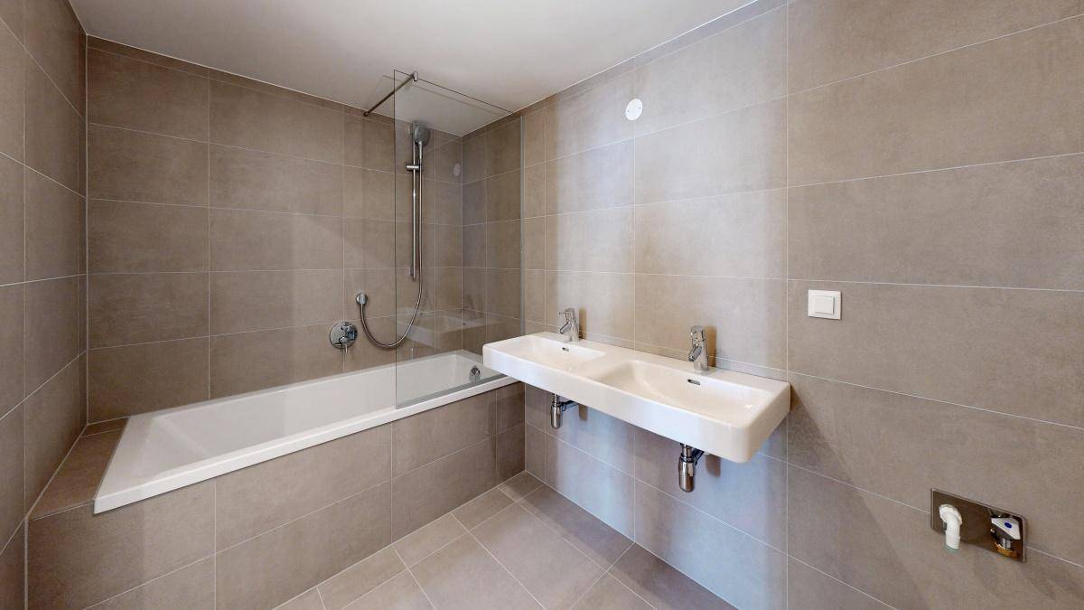 Modernes Badezimmer mit Doppelwaschbecken, Badewanne und grauen Fliesen.