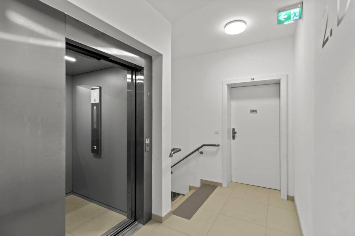 Heller Flur mit modernem Aufzug, Treppe und barrierefreier Rampe.