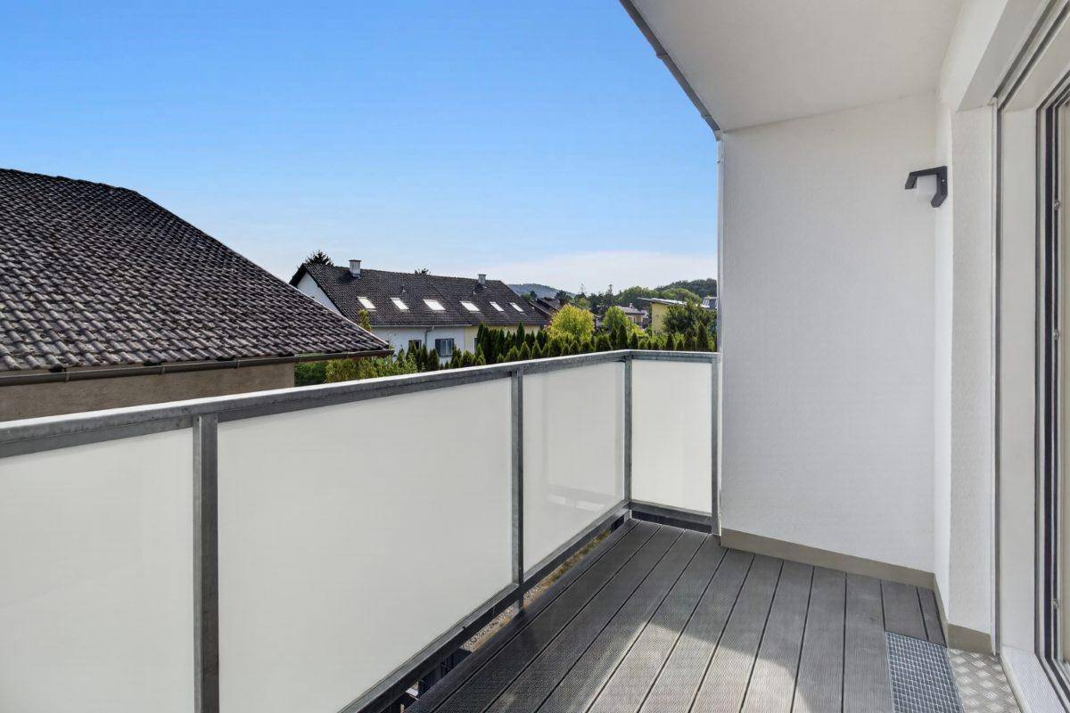 Heller Balkon mit Holzboden und Glasgeländer, bietet einen weiten Blick.