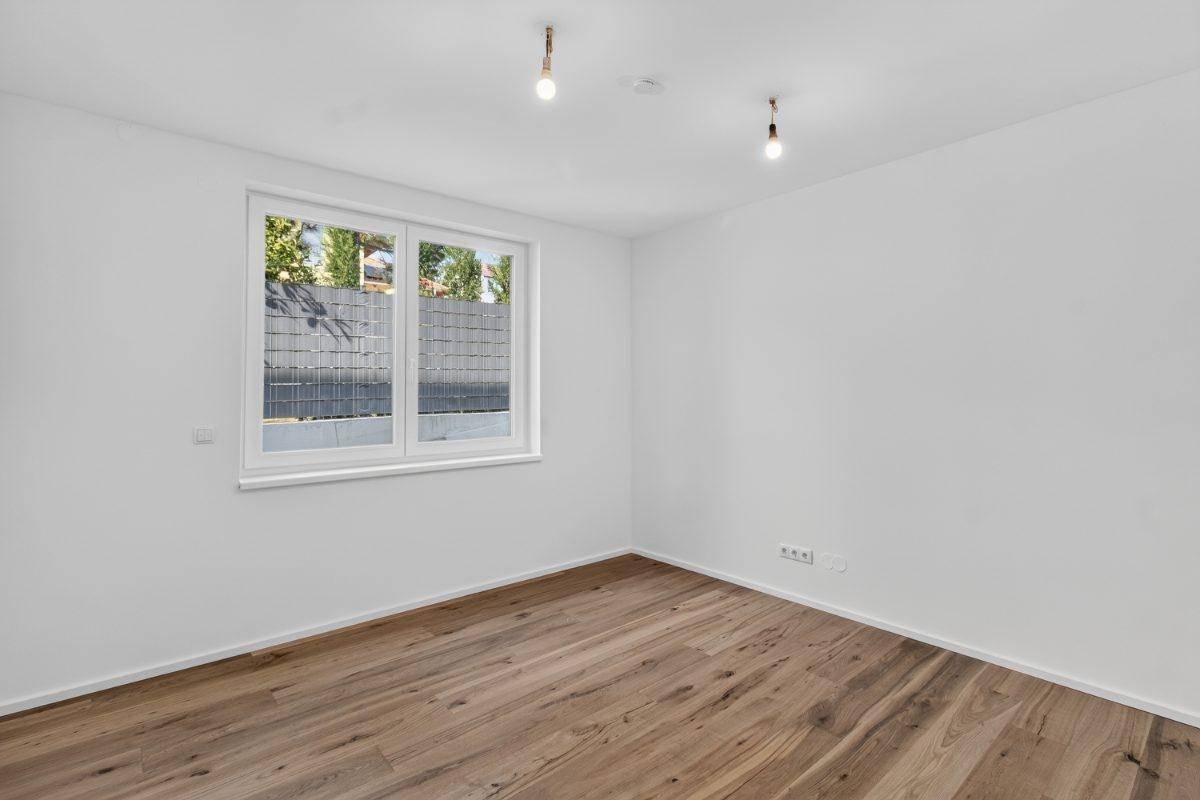 Helles Schlafzimmer mit Holzboden und Fenster, das viel Tageslicht hereinlässt.