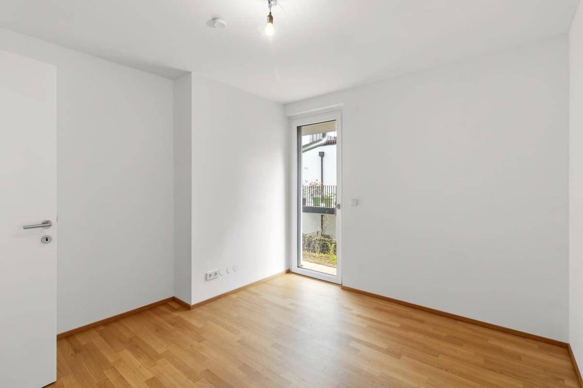 Helles Schlafzimmer mit Holzparkettboden und einem Fenster mit Blick ins Grüne.