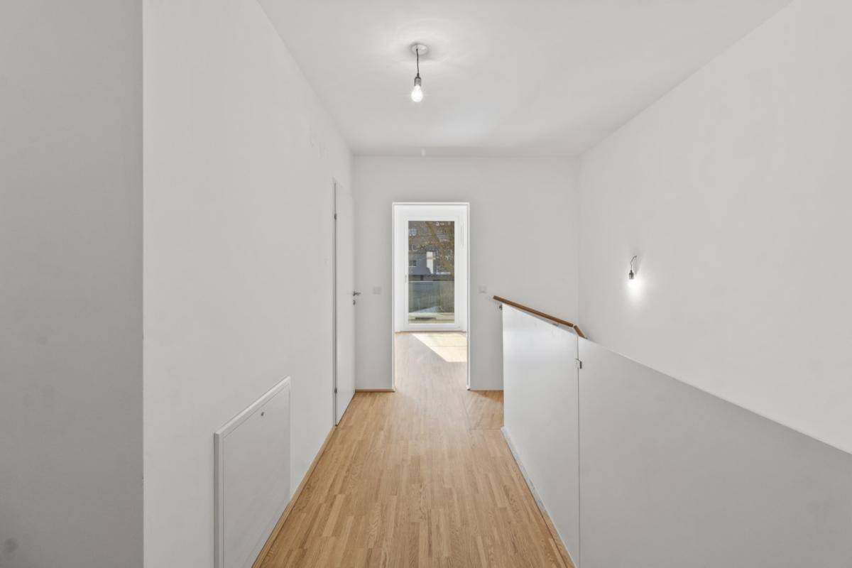 Heller Flur mit Holzboden und weiß gestrichenen Wänden, der zu weiteren Räumen führt.