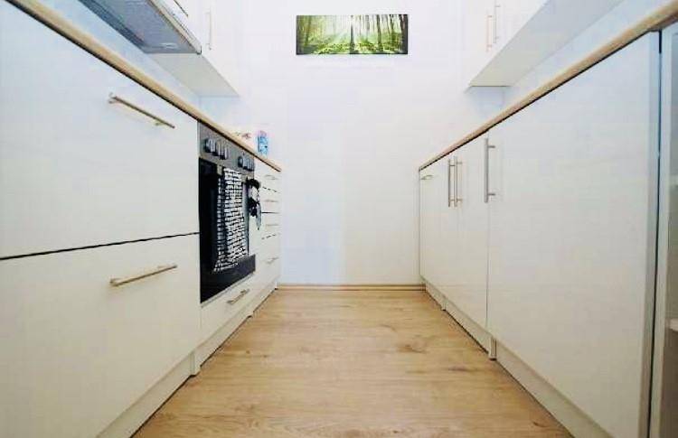 Schmale Küche mit weißen Schränken, Holz-Arbeitsplatten und hellem Laminatboden.
