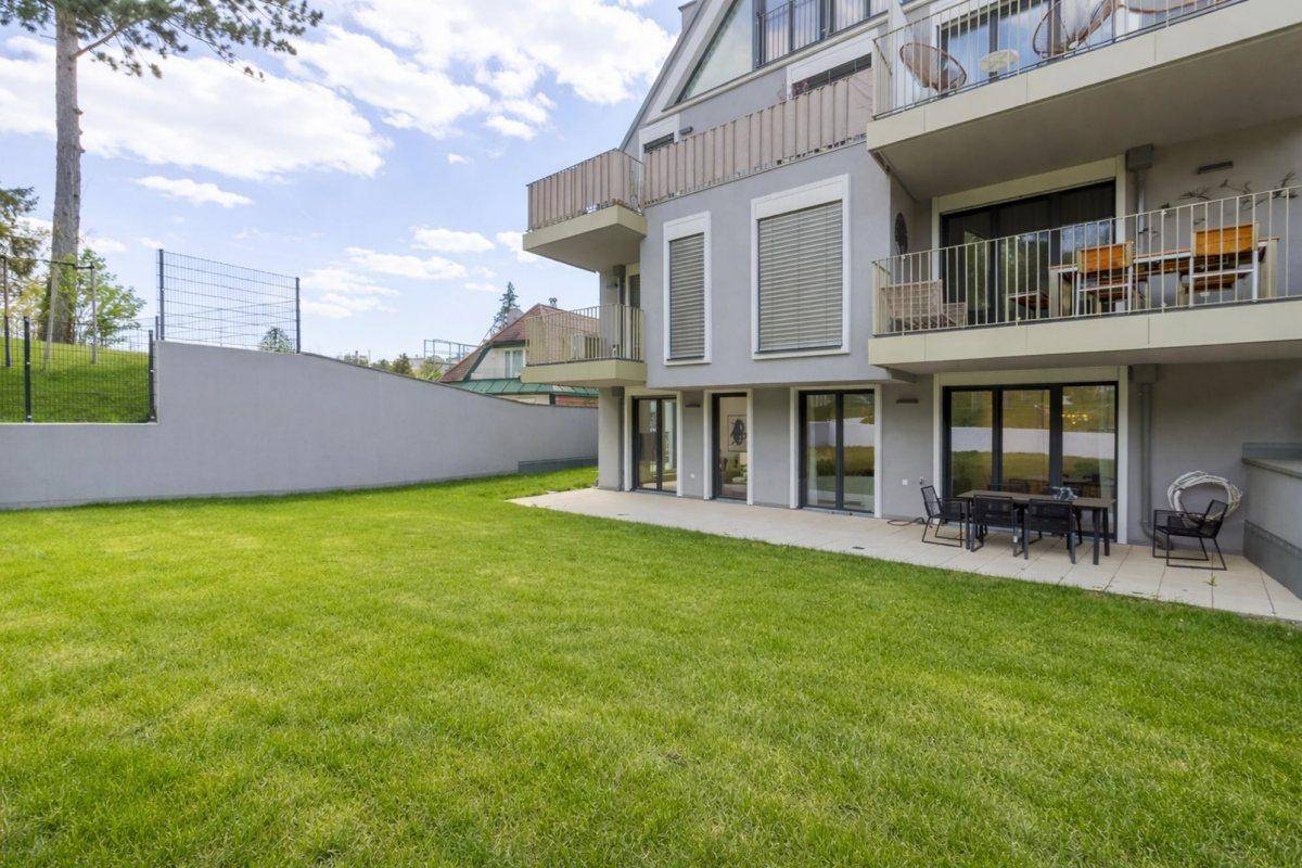 Weitläufiger Gartenbereich mit Rasenfläche und angrenzender Terrasse vor dem modernen Gebäude.