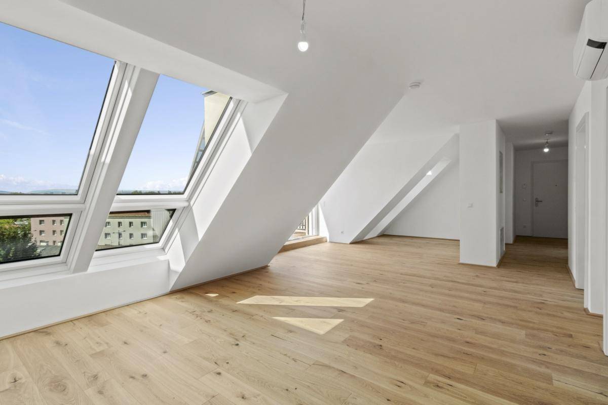 Heller Wohnraum im Dachgeschoss mit großen Dachfenstern, Holzboden und schrägen Wänden.
