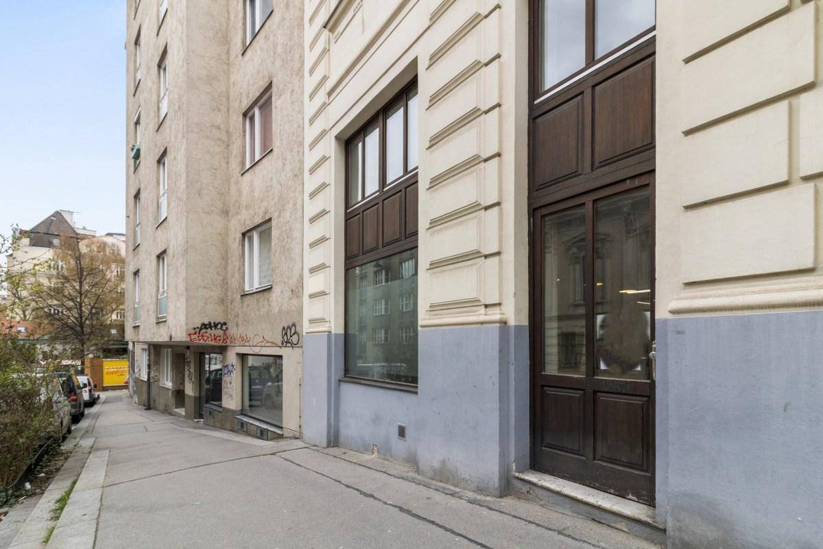 Seitenansicht eines Altbaus mit großen Fenstern und einem Gehweg entlang der Straße, der zum Eingang führt.