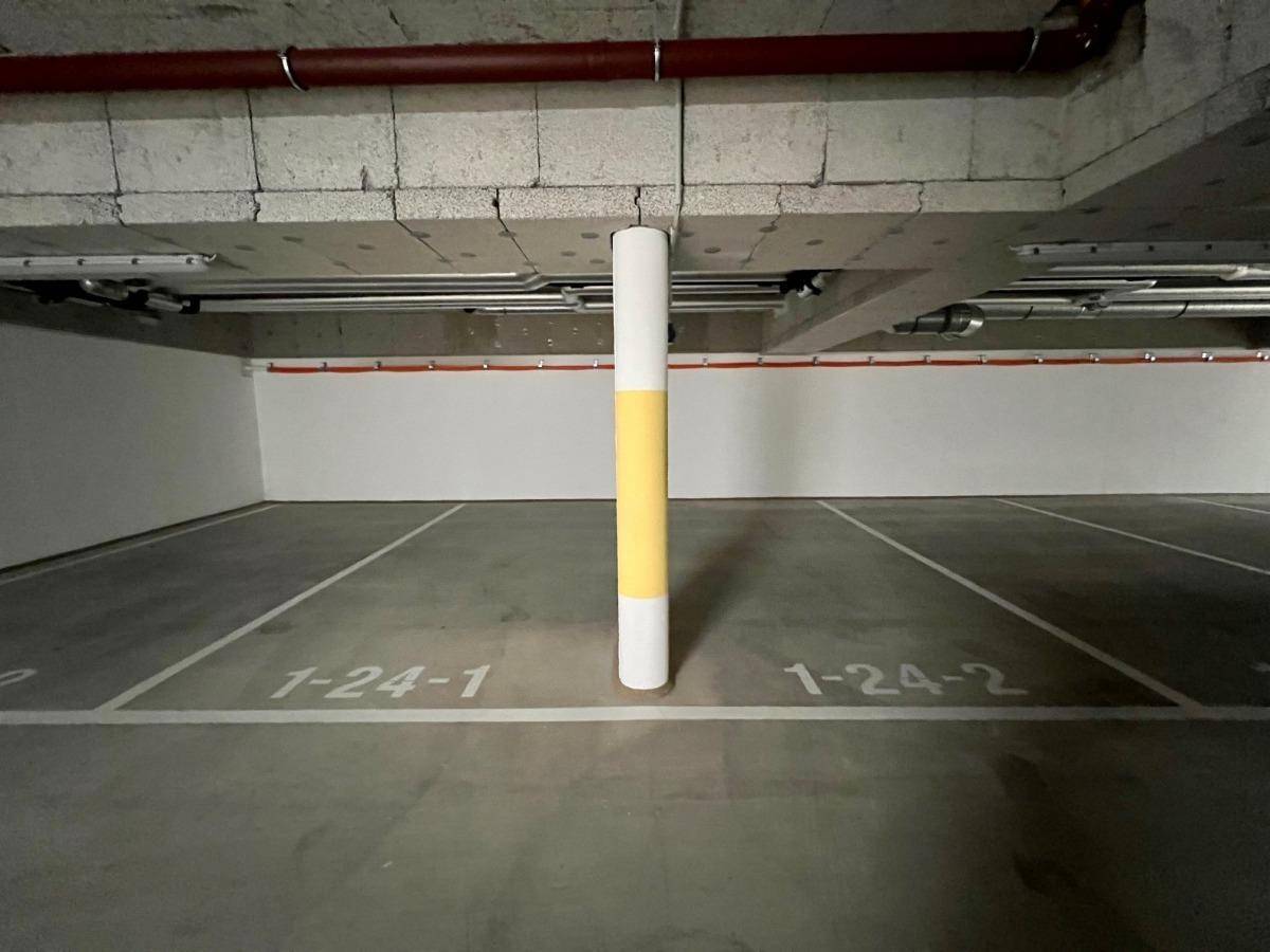 Leerer Parkplatz in der Tiefgarage mit einer gelb-weißen Säule und sichtbaren Betonstrukturen an der Decke.