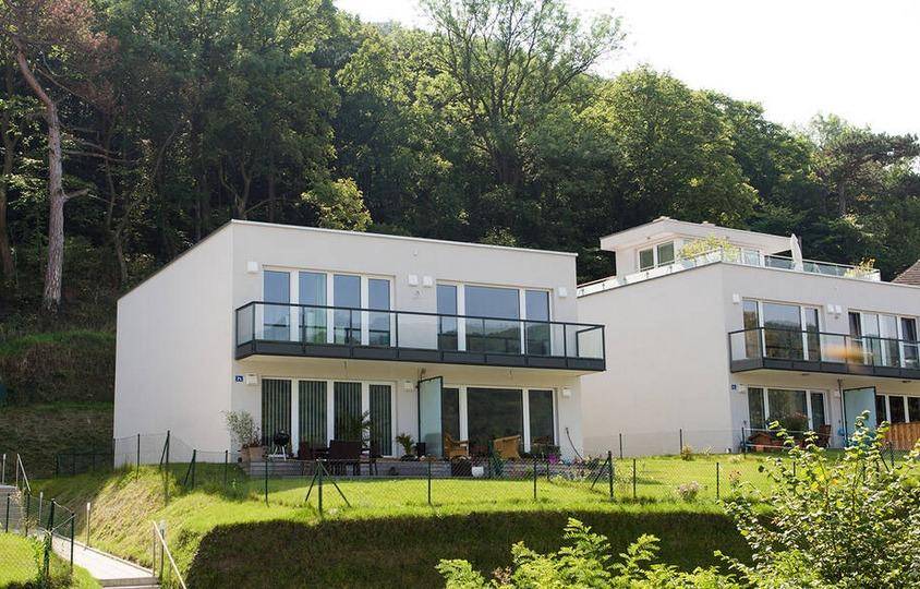 Zeitgenössische Wohngebäude mit großen Fenstern und Balkonen, umgeben von üppiger Natur und Hügeln.