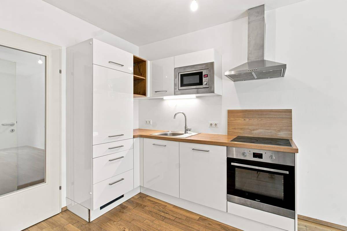 Moderne Einbauküche mit weißen Hochglanzfronten, Holz-Arbeitsplatte und integrierten Geräten.