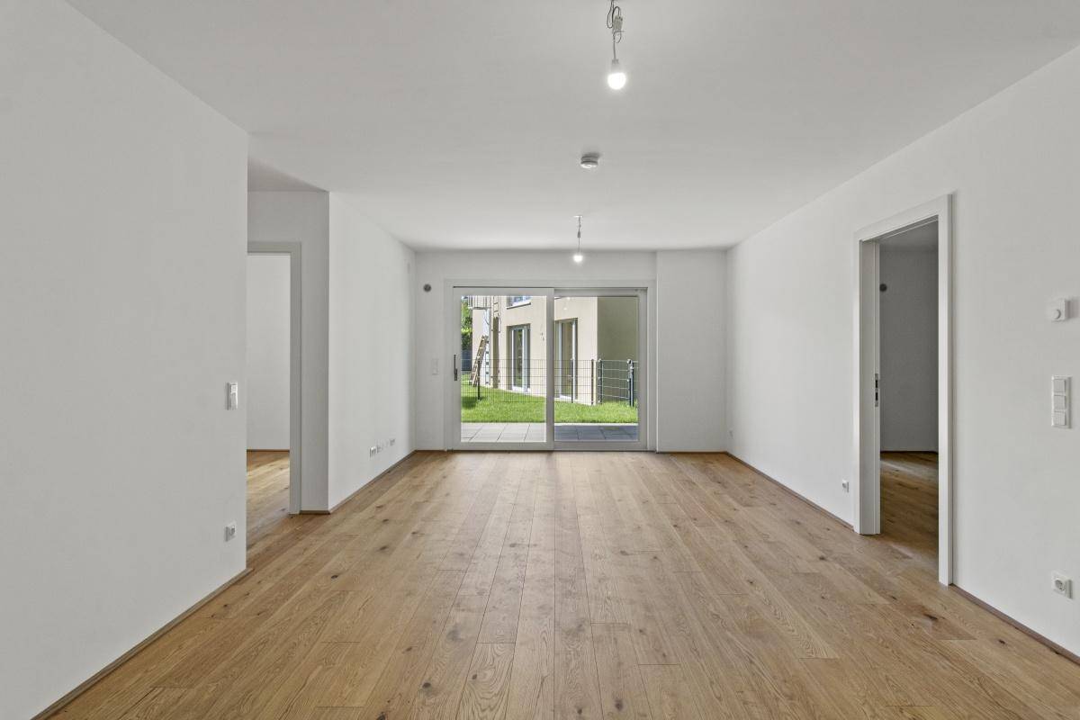 Geräumiges Wohnzimmer mit hellem Holzboden und direktem Zugang zur Grünfläche im Freien.