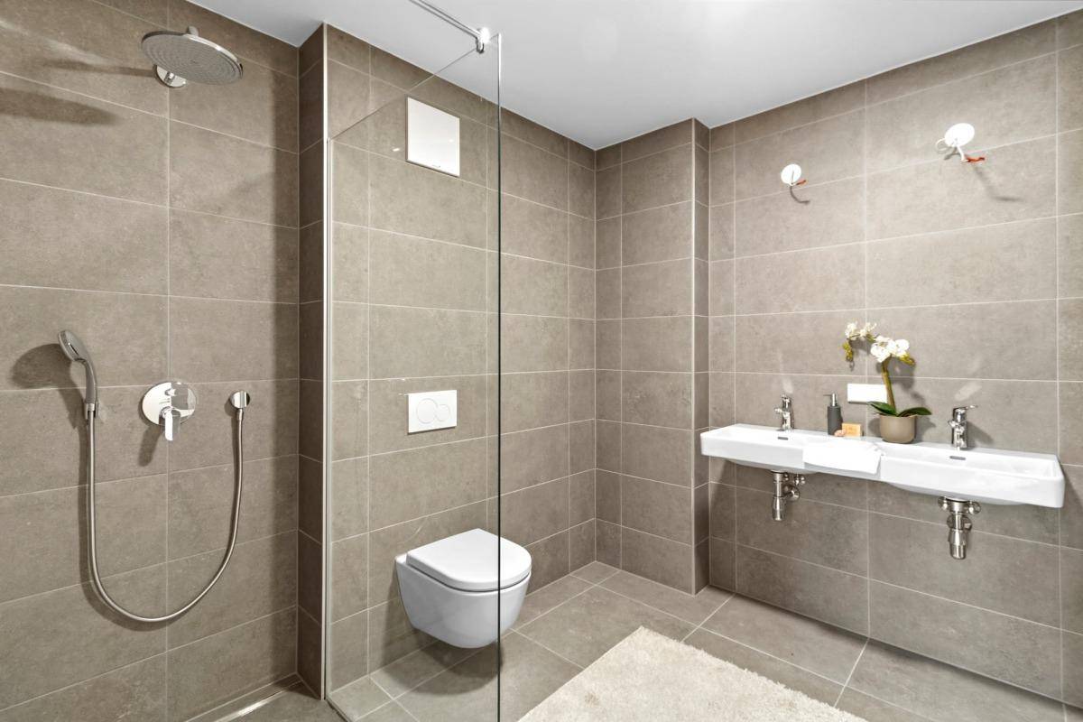 Modernes Badezimmer mit doppelten Waschbecken, großer Dusche und grauen Fliesen.