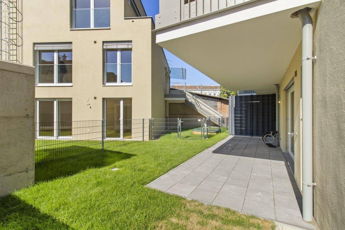 Terrasse mit Rasenfläche und Blick auf die moderne Architektur des Neubaus.