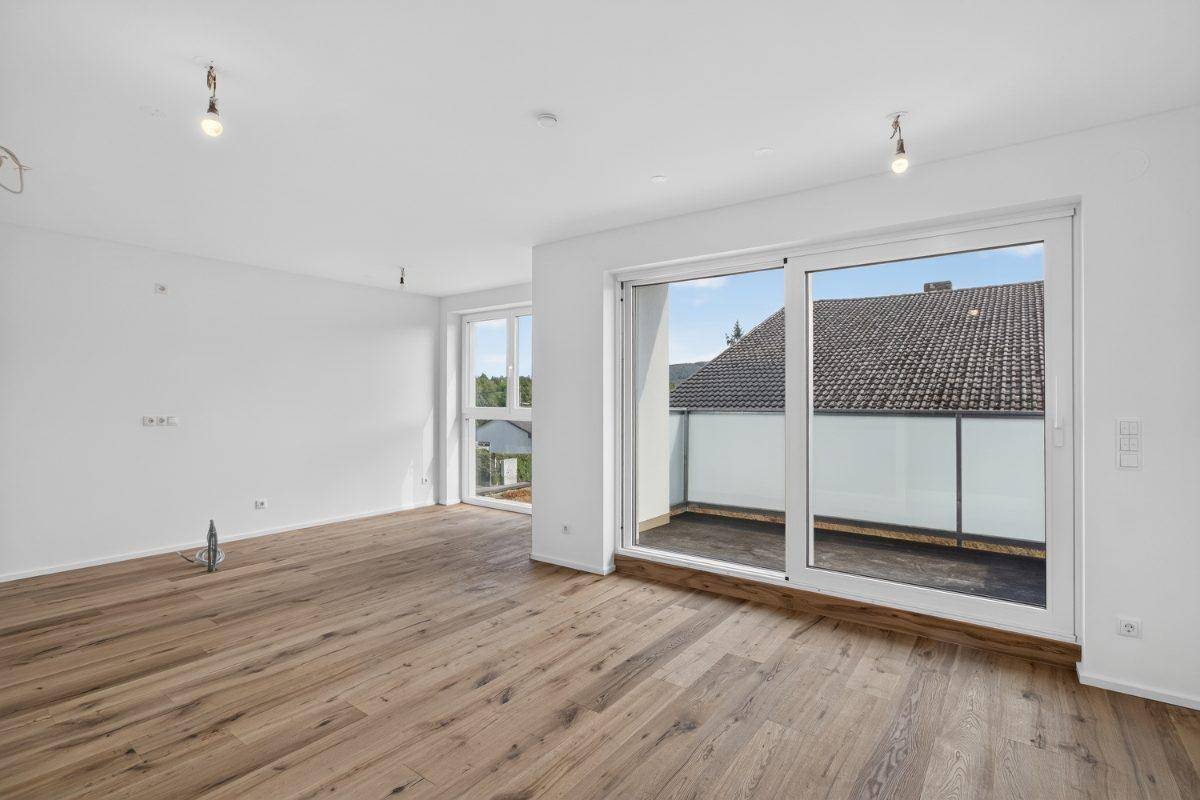 Heller, leerer Raum mit Holzboden und großem Schiebefenster zum Balkon.