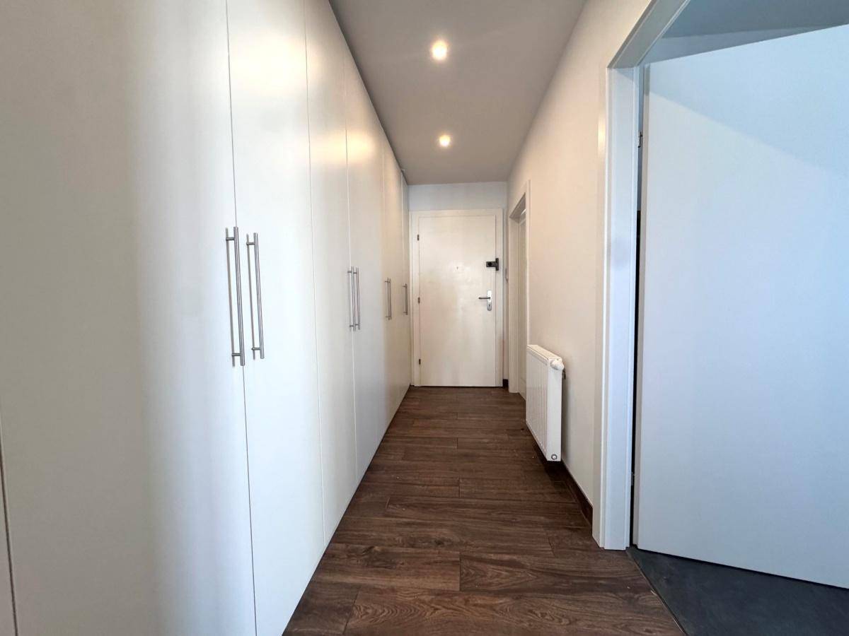Langer Flur mit integrierten weißen Einbauschränken und dunklem Holzboden für viel Stauraum.