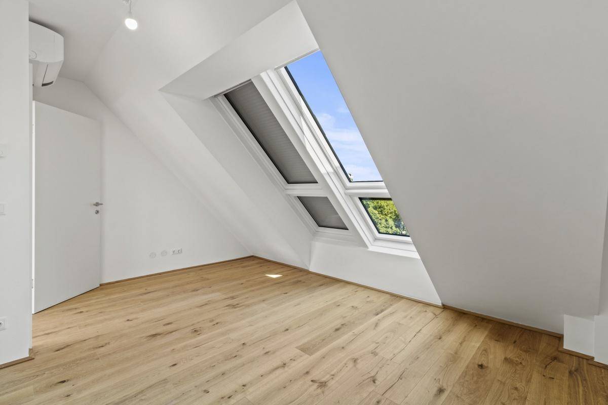 Dachgeschosszimmer mit Holzboden, Dachfenstern und Klimaanlage, bereit zum Einzug.