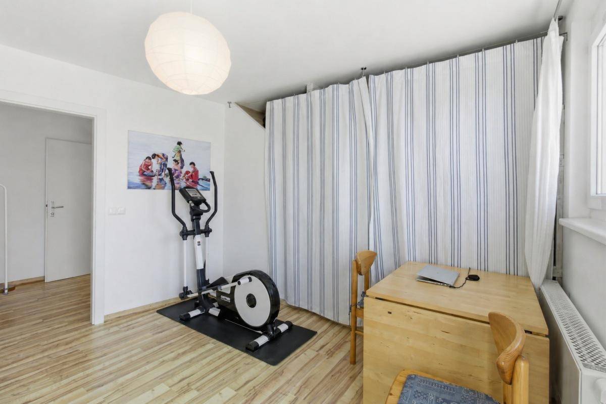 Helles Zimmer mit Laminatboden, Heimtrainer und Vorhängen, die einen Schlafbereich abtrennen.