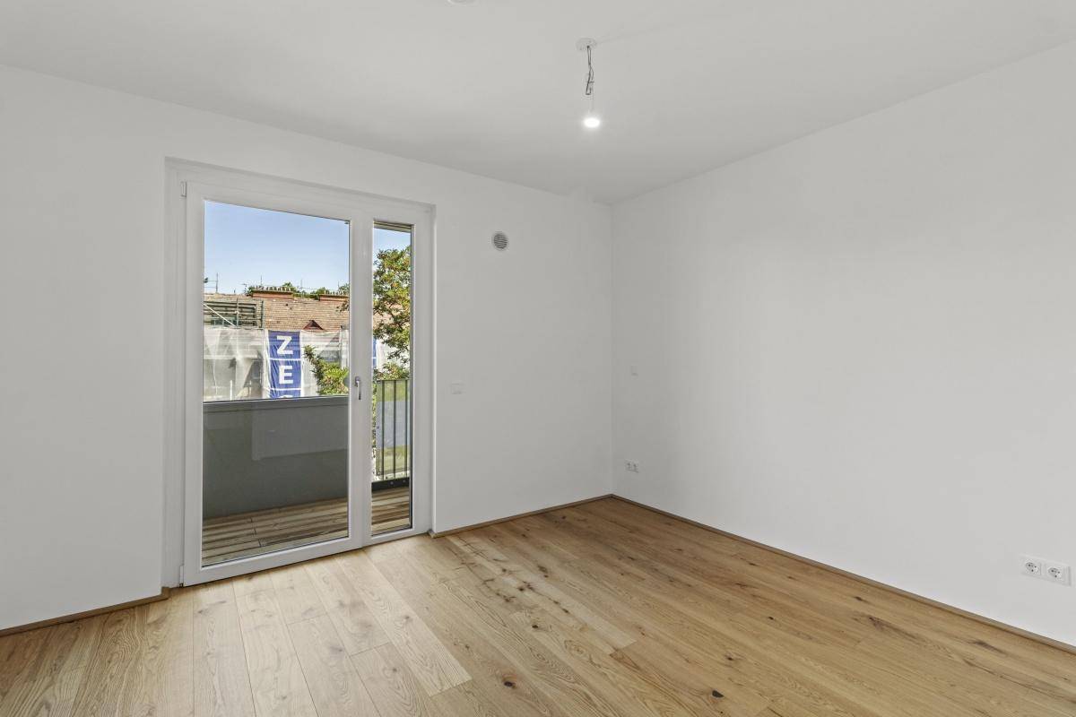 Unmöbliertes Zimmer mit Holzboden und Balkonzugang, bereit für die persönliche Gestaltung.