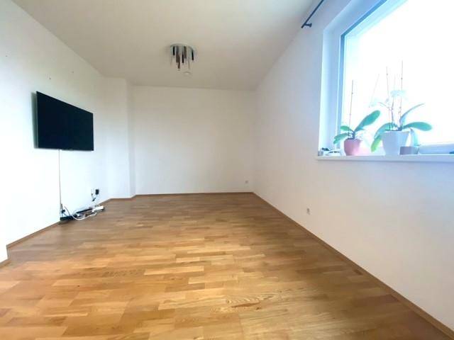 Geräumiges Wohnzimmer mit hellem Parkettboden und einem großen Fenster, das viel Licht hereinlässt.
