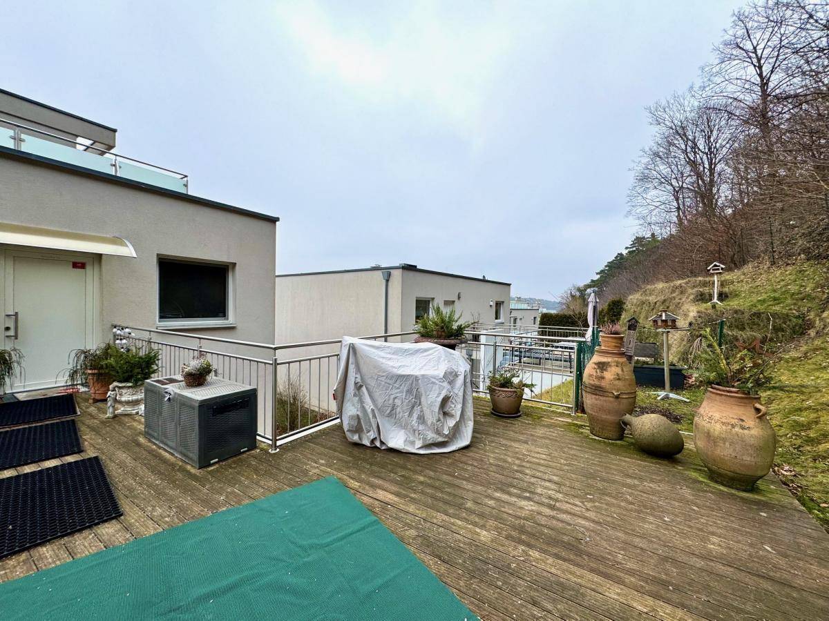 Weitläufige Holzterrasse mit Blick auf die umliegende Hügellandschaft und weitere Gebäude.