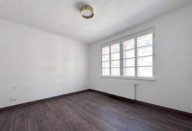 Kleineres, helles Zimmer mit dunklem Holzboden und einem Fenster, geeignet als Schlaf- oder Arbeitszimmer.