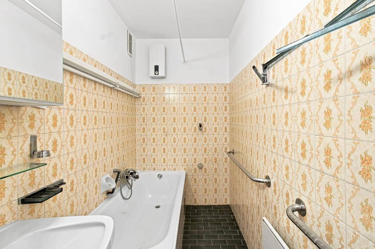 Badezimmer mit Badewanne und gemusterten Wandfliesen, ausgestattet mit Haltegriffen.