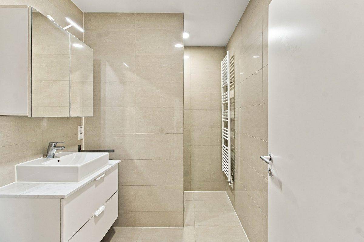 Helles Badezimmer mit beigen Fliesen, modernem Waschtisch und praktischem Spiegelschrank.