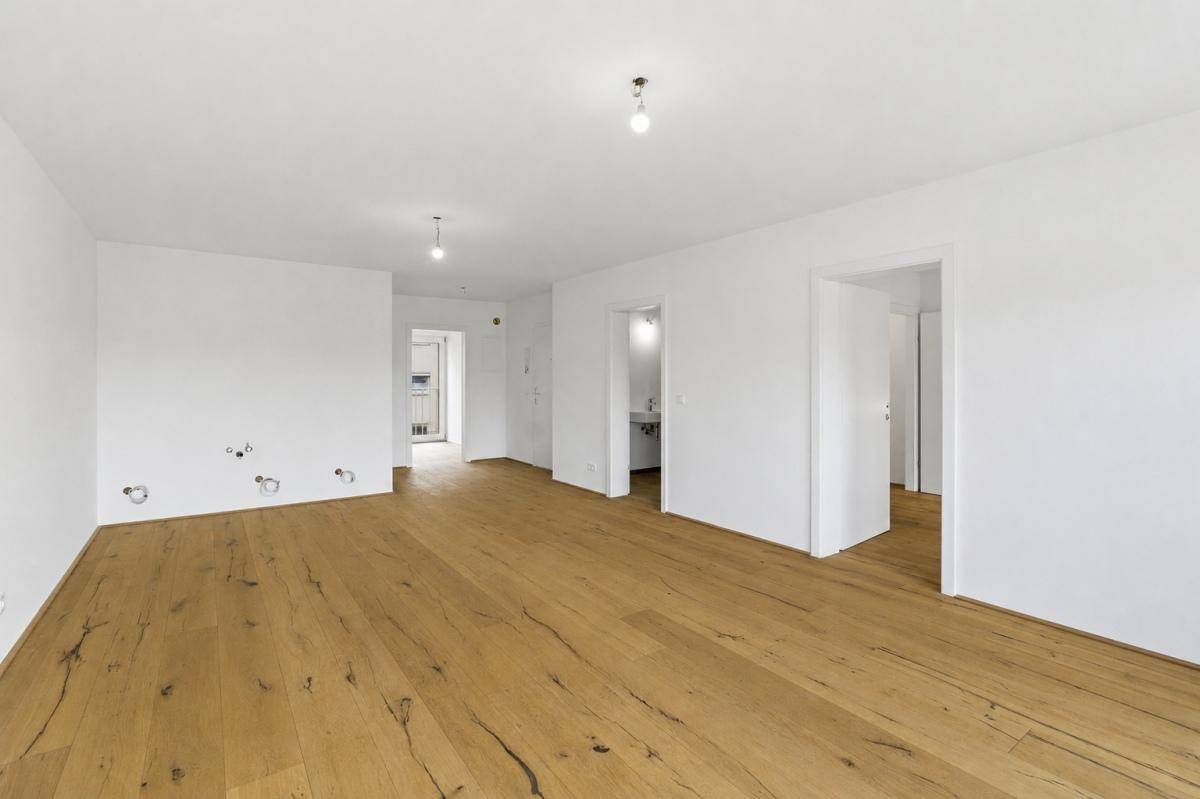 Heller Raum mit neuem Holzfußboden und weißen Wänden, bereit für die Einrichtung.