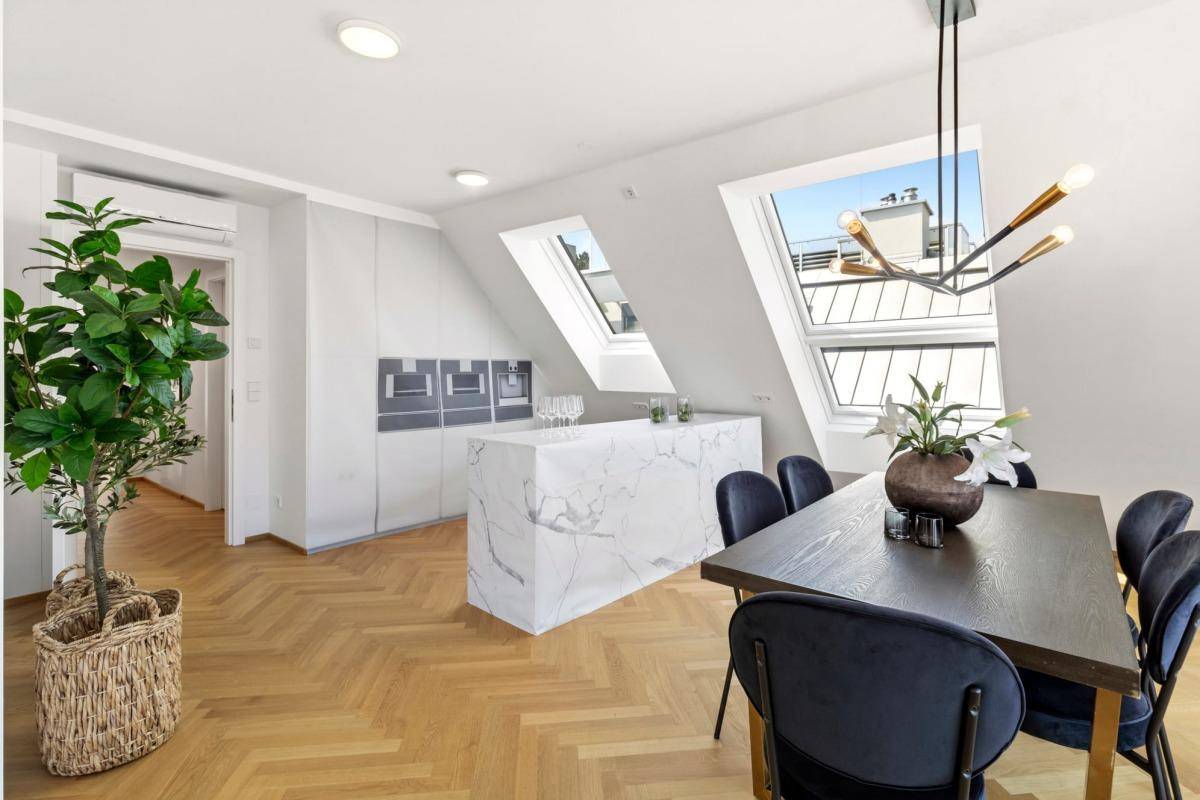 Moderne Küche mit Marmorinsel und Essbereich unter Dachschrägen mit großen Dachfenstern.